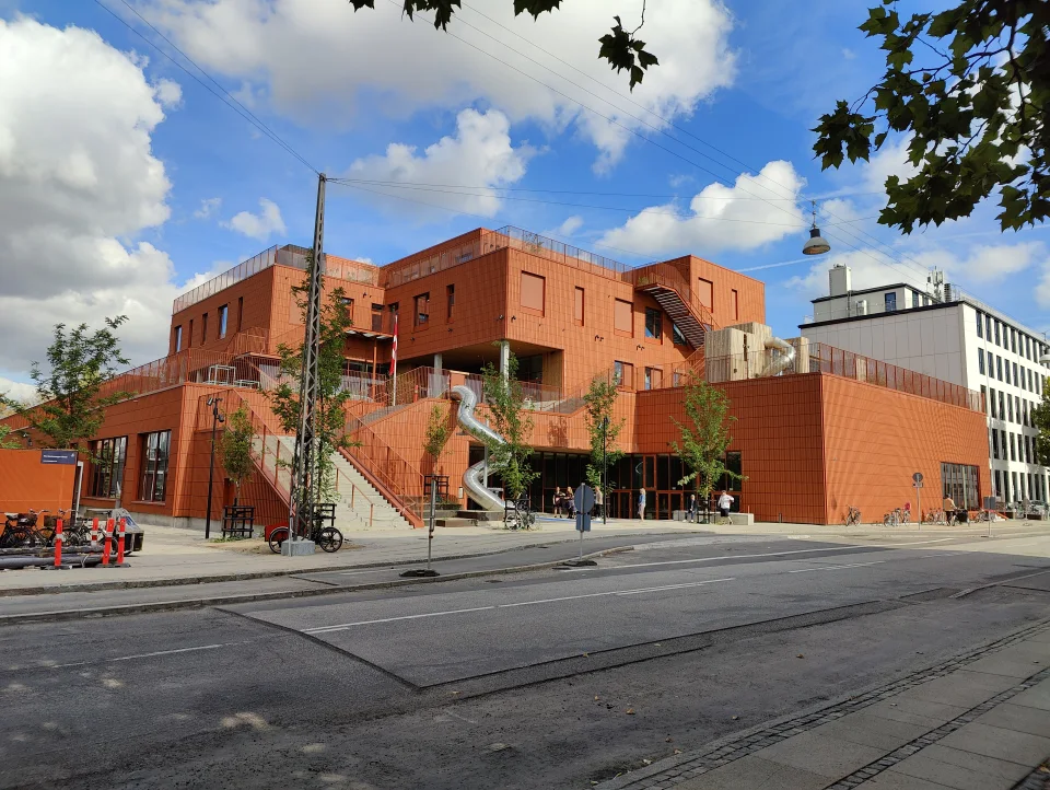 Nybygget skole med rødt teglfacade, udendørs trapper og rutsjebane mellem etagerne